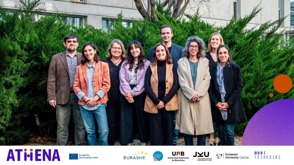 Skupinová fotografie členů mezinárodního projektu ATHENA pořízená venku před budovou Universitat Autònoma de Barcelona. Devět osob stojí v řadě před zelenými keři, v pozadí je vidět část univerzitní budovy. Ve spodní části fotografie jsou loga zapojených organizací: ATHENA, Evropská unie, EURASHE, European Disability Forum, Universitat Autònoma de Barcelona, Johannes Kepler Universität Linz, European University Cyprus a Masarykova univerzita – Středisko Teiresiás.